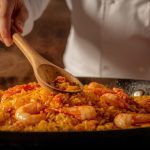Chef stirring a pan of seafood paella with a wooden spoon