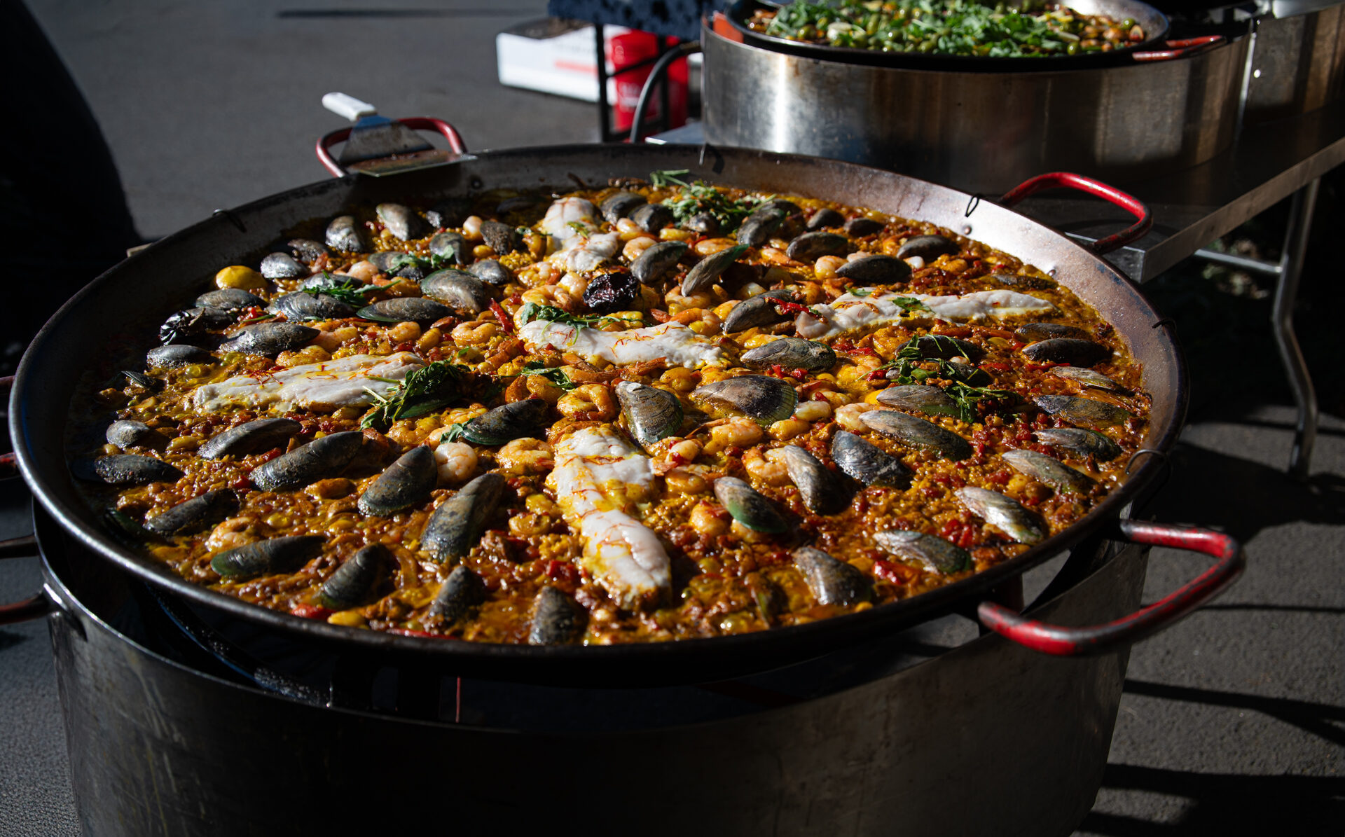 A wide steel pan of paella with mussels, seafood and greens.