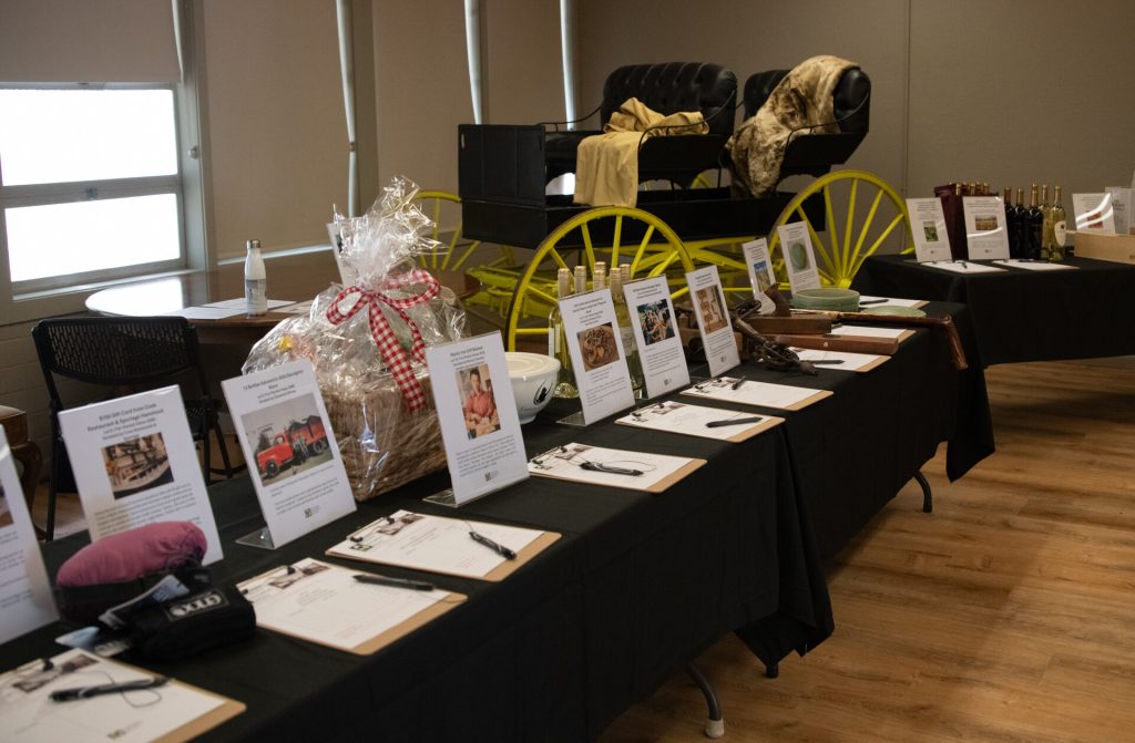 A long table of wrapped gift baskets and bid sheets for the silent auction.