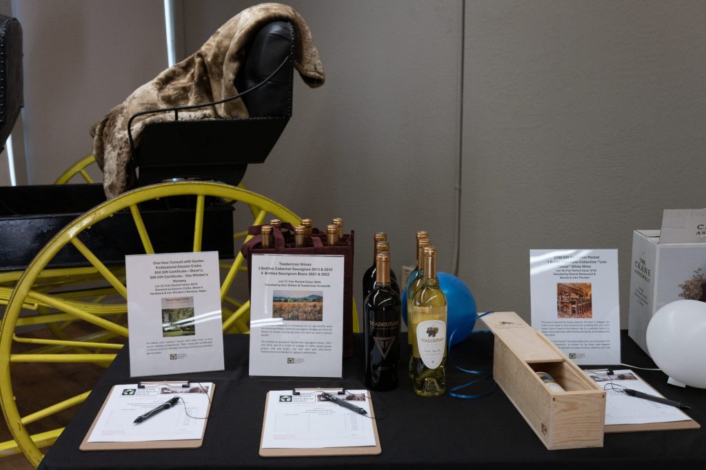 Silent auction items and wine bottles displayed beside a yellow antique carriage wheel.