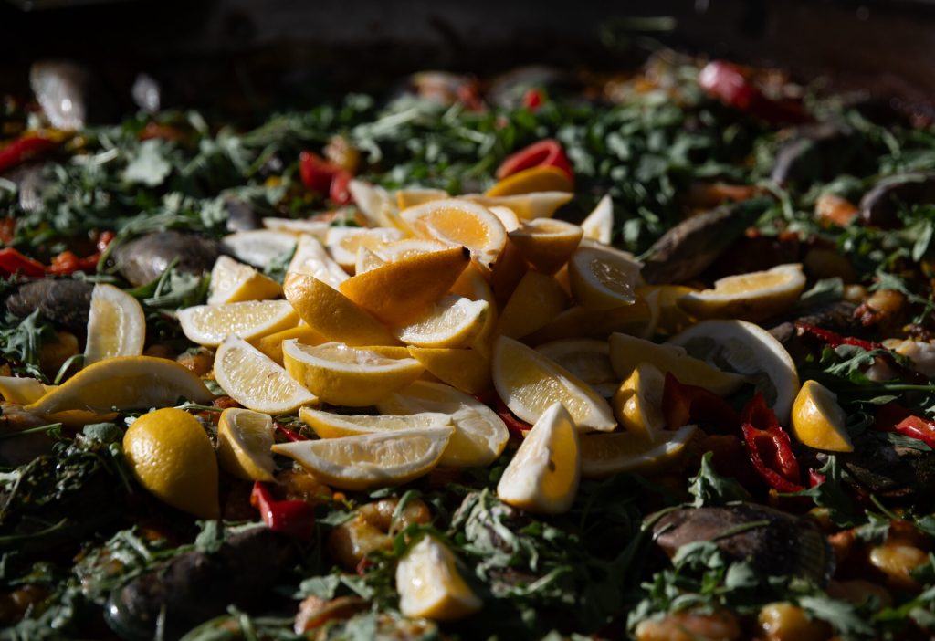 Close-up of paella topped with lemon wedges, mussels and greens.