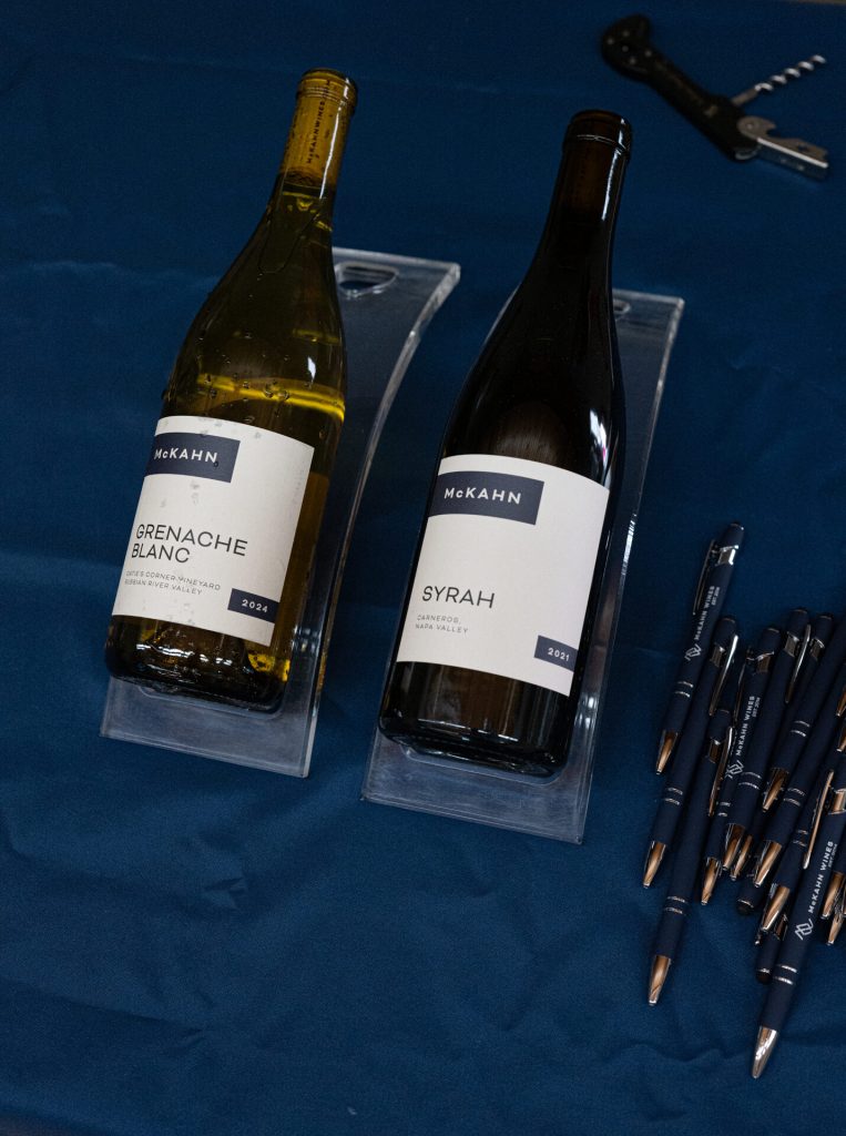 Two bottles of McKahn wine, a Grenache Blanc and a Syrah, displayed on blue cloth.